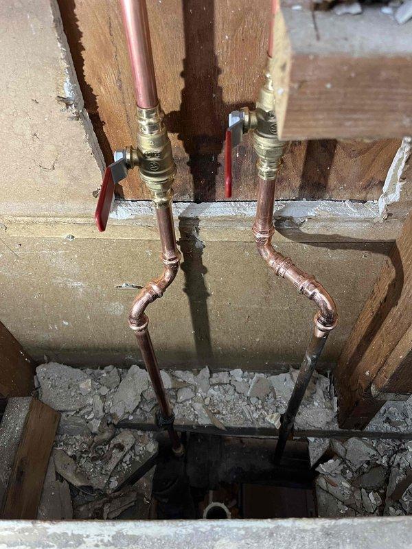 Completed shower valve replacement in a bathroom under renovation. Installed new copper supply lines with brass shut-off valves featuring red handles on exposed wall framing. Properly secured all connections and verified operation after installation.
