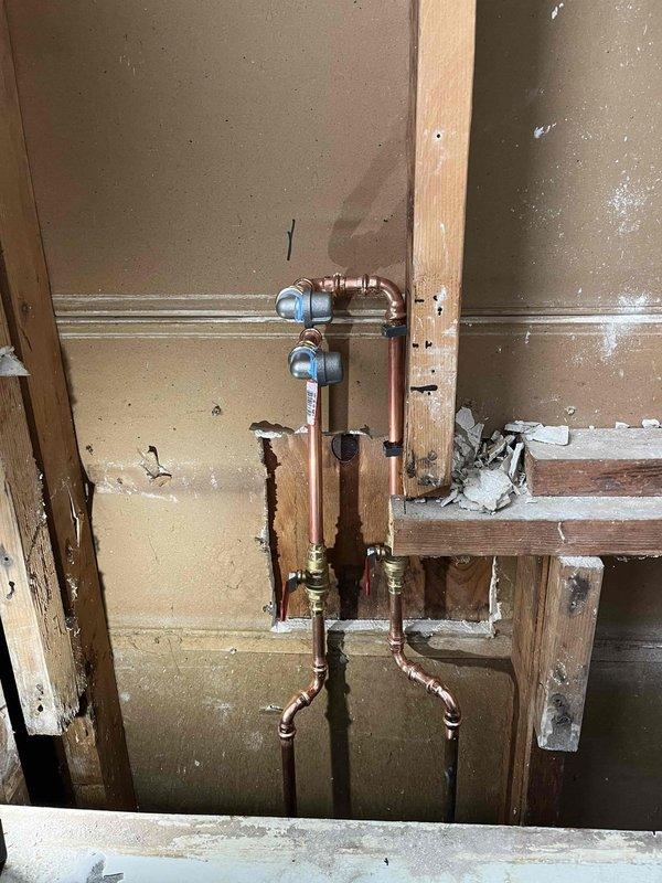 Completed shower valve replacement in a bathroom under renovation. Installed new copper supply lines with brass shut-off valves featuring red handles on exposed wall framing. Properly secured all connections and verified operation after installation.