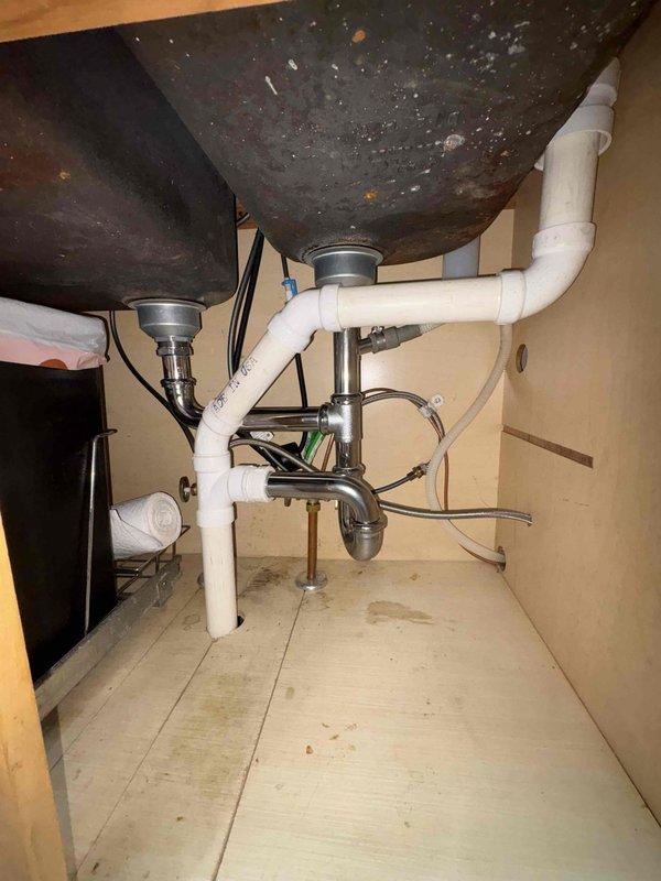 Repaired leaking sink drain by updating tubular components to match existing fixtures and ensure proper drainage. Raised the Air Admittance Valve (AAV) to comply with current plumbing code requirements. Lowered the 90-degree elbow under kitchen sink to establish correct drain pitch, eliminating previous water damage issues evident from cabinet staining.