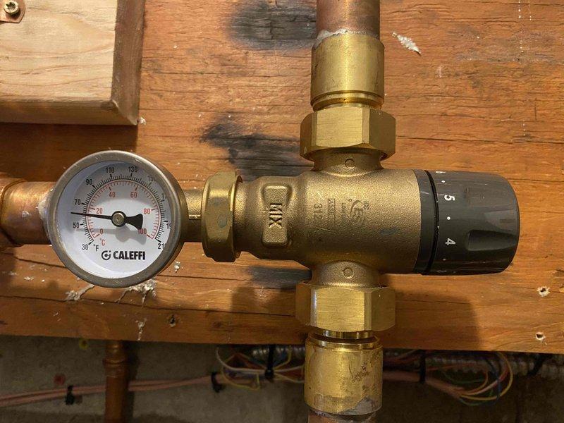 Inspected radiant floor heating system in response to customer's concerns about insufficient heat output. Observed Caleffi mixing valve assembly and temperature gauge reading approximately 40-45°F (100°F on secondary gauge), significantly below optimal operating temperature for radiant floor heating. Adjusted temperature regulation settings on mixing valve to increase system output and improve heating efficiency.