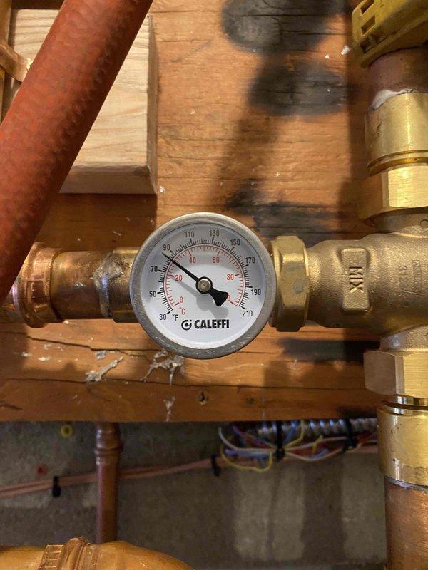 Inspected radiant floor heating system in response to customer's concerns about insufficient heat output. Observed Caleffi mixing valve assembly and temperature gauge reading approximately 40-45°F (100°F on secondary gauge), significantly below optimal operating temperature for radiant floor heating. Adjusted temperature regulation settings on mixing valve to increase system output and improve heating efficiency.