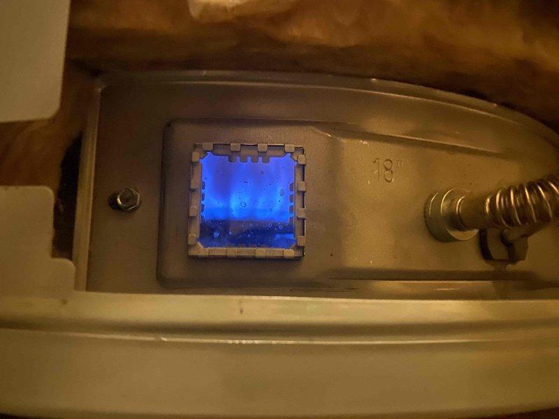 Serviced gas water heater with blue indicator light operational on control panel. Inspected and verified proper function of gas shut-off valve with red handle. No leaks detected during inspection; system operating within normal parameters.