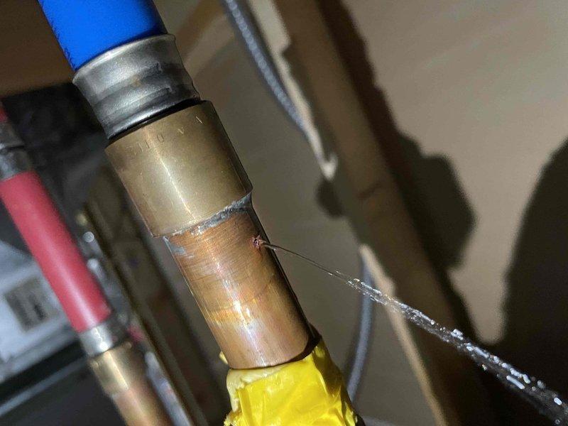 Responded to emergency service call for a 15-year-old leaking hot water tank. Diagnosed leak at copper pipe connection with brass fitting near the expansion tank installation. Repaired compromised joint and inspected surrounding plumbing components within the wall cavity to ensure system integrity.