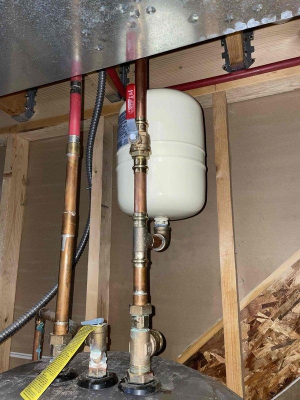 Responded to emergency service call for a 15-year-old leaking hot water tank. Diagnosed leak at copper pipe connection with brass fitting near the expansion tank installation. Repaired compromised joint and inspected surrounding plumbing components within the wall cavity to ensure system integrity.
