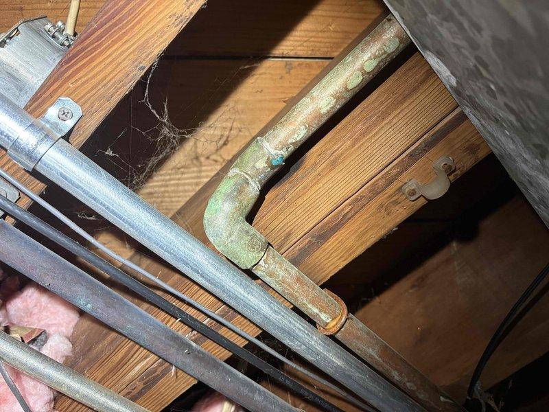 Responded to water leak complaint and conducted thorough inspection of plumbing system. Identified corroded pipe fitting in crawl space above water heater area showing significant oxidation and moisture damage. Documented conditions of water heater installation and overhead plumbing infrastructure, photographed deteriorated metal elbow joint with visible corrosion and patina indicating chronic leak source. Provided comprehensive assessment and no-charge estimate for necessary repairs.