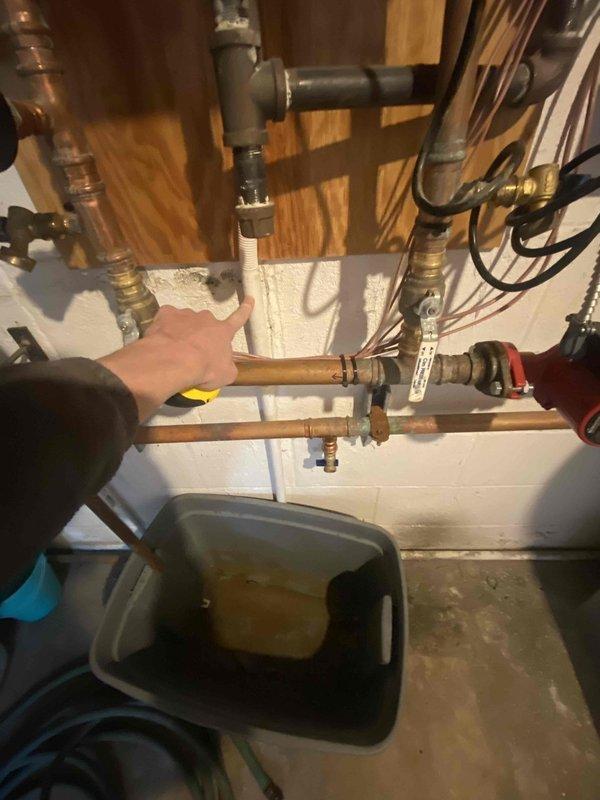 Completed estimate for combi boiler system replacement in residential basement utility room. Assessed existing copper piping infrastructure including four vertical supply lines with red-handled shut-off valves, expansion tank, and multiple horizontal distribution lines mounted to ceiling joists and concrete block walls. Evaluated current plumbing configuration, pipe routing, and connection points to determine scope of work for new combination boiler installation and integration with existing hydronic heating system.