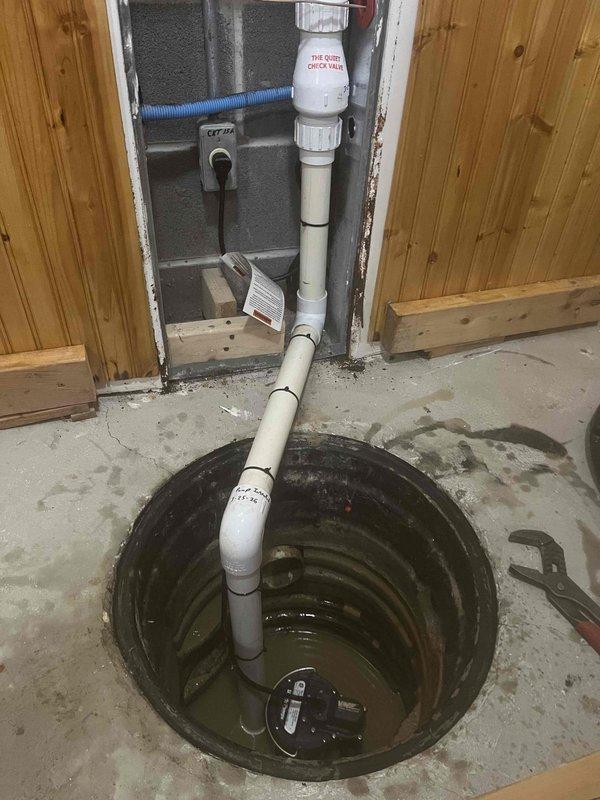 Completed sump pump installation in basement crawl space with concrete floor. Cut 18-24 inch diameter sump pit into existing concrete foundation, installed submersible sump pump unit, and ran white PVC discharge piping vertically through wood-framed wall opening to exterior drainage point. Secured discharge pipe with proper mounting and labeled system per code requirements. Tested pump operation and verified proper water level activation and discharge flow.