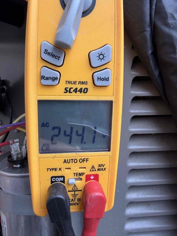 Completed cooling maintenance club visit on residential HVAC system. Performed electrical diagnostics using multimeter, measuring 244.1 VAC at the unit, confirming proper voltage supply to the system. Inspected condensate drain assembly including P-trap, PVC drainage lines, and safety float switch with red shut-off valve, all found to be functioning properly with no blockages detected.