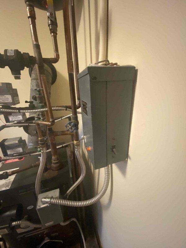 Performed on-site evaluation of existing oil-fired boiler system for conversion to electric air handler. Assessed current mechanical installation including boiler unit, copper piping distribution, control valves, and electrical infrastructure. Documented existing equipment configuration with multiple pipe connections, brass fittings, and electrical conduit routing to panel box. Evaluated wall-mounted components and system layout to determine requirements for electric heating conversion. Provided estimate for removal of oil boiler system and installation of electric air handler unit.