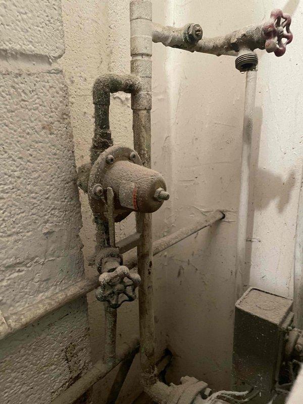 Responded to service call for boiler producing popping, banging, and gurgling noises. Upon inspection, found aging boiler system estimated at minimum 20 years old with significant corrosion and mineral buildup visible on plumbing components and piping assembly. Examined gas-fired heating appliance with ceramic log configuration and verified proper flame pattern with blue base flames and yellow-orange tips. Assessed heavily corroded piping, trap assembly, and valve components showing extensive rust staining and deterioration throughout the system. Noted mineral deposits and moisture damage consistent with long-term operation. Discussed digital thermostat upgrade options with customer for improved temperature control and system efficiency. Documented system condition with photographs for service records.