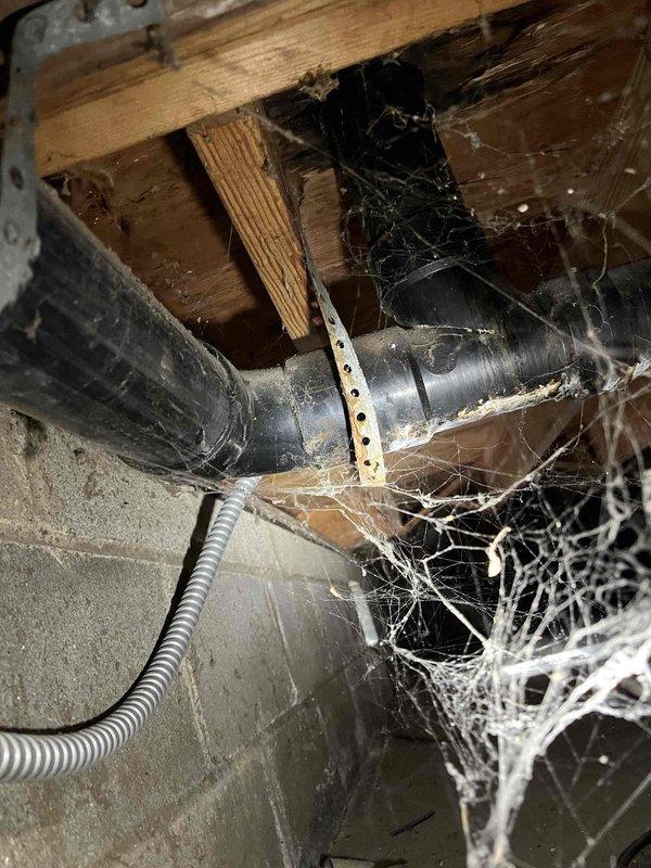 Completed routine plumbing membership inspection of residential property, examining both crawlspace plumbing infrastructure and bathroom fixtures. Inspected exposed piping in basement area, including gray supply lines secured with metal hangers, flexible conduit connections, and verified structural mounting points beneath floor joists. Evaluated modern bathroom shower enclosure featuring frameless glass door system, marble-effect tile surround, recessed storage niche, and wall-mounted handheld shower fixture with black mounting hardware, confirming all plumbing fixtures and connections were functioning properly with no visible leaks or immediate concerns noted.