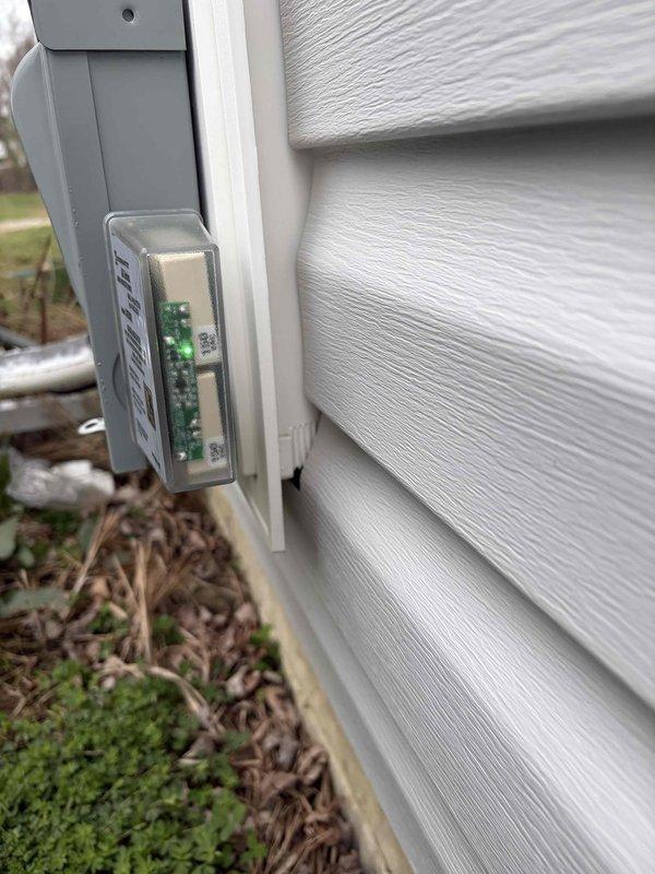 Installed residential surge protection device on exterior of home. Unit mounted to building siding with green LED indicators operational and functioning properly to monitor power status and surge protection capability.