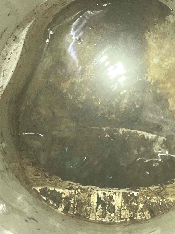 Responded to emergency call for sewage backup in residential property. Upon arrival, inspected backflow prevention device due to customer concern about potential obstruction. Investigation revealed significant accumulation of sewage and debris within the backflow assembly chamber. Interior walls showed extensive staining and residue buildup consistent with recent backup event. Dark wastewater was pooled at base of device, and interior surfaces displayed deterioration including flaking coating material and corrosion around sealing edges. Documented condition of backflow device interior showing heavy contamination and mineral deposits from prolonged exposure to sewage. Identified backflow device as source of backup issue requiring immediate attention to restore proper drainage function and prevent future sewage intrusion into residence.