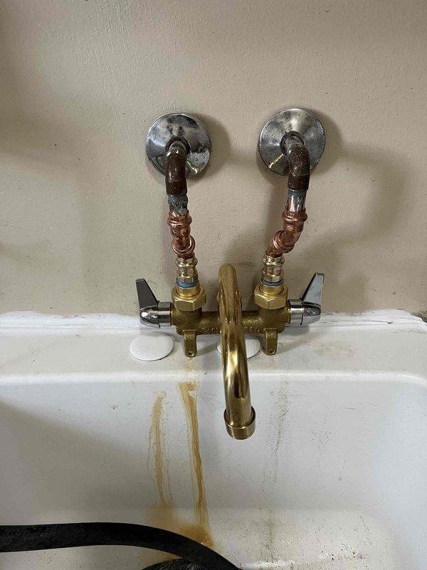 Responded to a leak at a utility sink in the laundry room. Upon inspection, found an older wall-mounted faucet assembly with exposed copper supply lines connected to brass shut-off valves. Identified the source of the leak, performed necessary repairs to the faucet stems and valve connections, and verified all water supply connections were properly sealed and functioning without leakage.