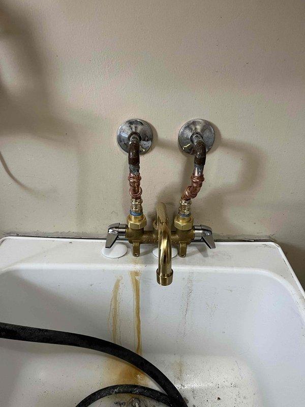 Responded to a leak at a utility sink in the laundry room. Upon inspection, found an older wall-mounted faucet assembly with exposed copper supply lines connected to brass shut-off valves. Identified the source of the leak, performed necessary repairs to the faucet stems and valve connections, and verified all water supply connections were properly sealed and functioning without leakage.