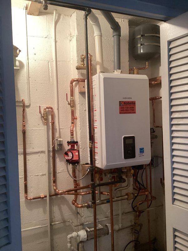 Completed installation of Navien tankless boiler system in utility area. Configured complete hydronic heating system with copper piping network, installed expansion tank, integrated red-handled isolation valves throughout system for service accessibility, and mounted circulation pump. System commissioned and verified operational at 122°F heating mode with 217 PSI operating pressure, space heating zone 1 active, and domestic hot water mode disabled per system requirements.