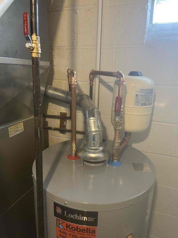 Completed water heater upgrade from traditional tank-style unit to tankless system. Removed existing cylindrical tank water heater and installed new Lochinvar tankless unit with proper copper piping connections, valve assembly with temperature controls, and integrated expansion tank. Ensured all connections met code requirements and system was tested for proper operation and leak-free performance.