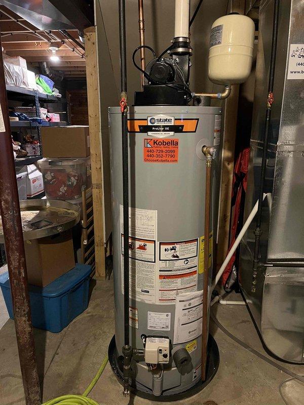 Responded to service call for an 11-year-old 50-gallon gas power-vented water heater experiencing leaks from both top and bottom connections. Inspected unit and confirmed active leaking, instructed property owner to shut off cold water supply valve to tank and open hot water taps throughout home to relieve pressure and prevent flooding. Documented existing State brand water heater with power vent assembly, expansion tank, and associated plumbing connections showing signs of age-related deterioration requiring replacement.