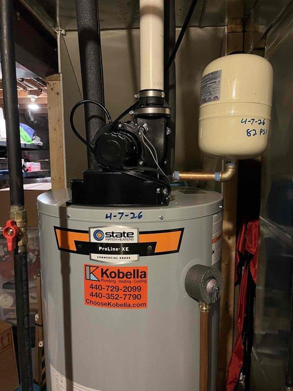 Responded to service call for an 11-year-old 50-gallon gas power-vented water heater experiencing leaks from both top and bottom connections. Inspected unit and confirmed active leaking, instructed property owner to shut off cold water supply valve to tank and open hot water taps throughout home to relieve pressure and prevent flooding. Documented existing State brand water heater with power vent assembly, expansion tank, and associated plumbing connections showing signs of age-related deterioration requiring replacement.