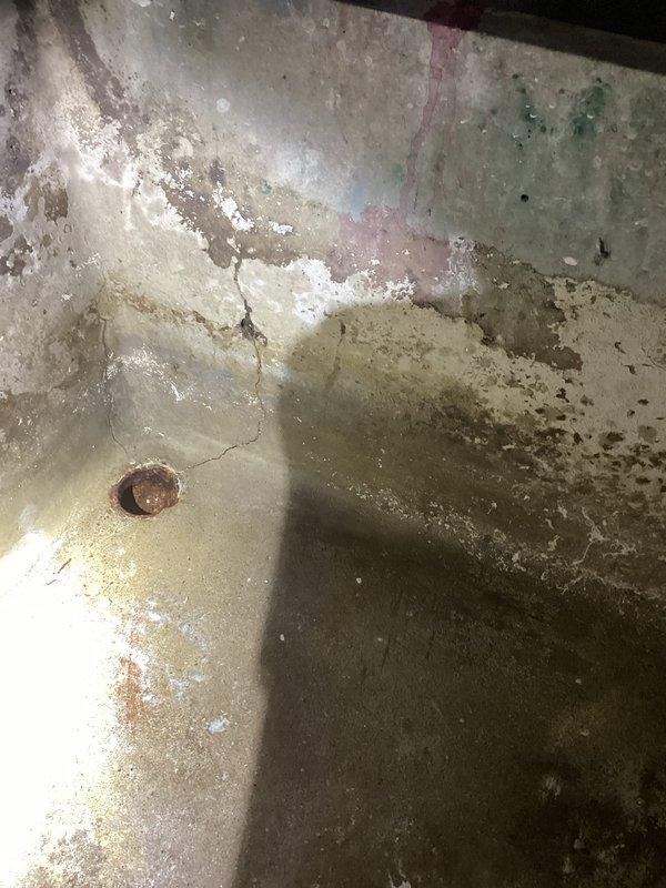 Responded to service call for non-operational sump pump in laundry area. Upon inspection, found sump pump basin located in basement utility space with evidence of significant moisture exposure and deteriorated conditions. Basin showed extensive corrosion, mineral deposits, and surface degradation indicating prolonged water contact and lack of maintenance. Pump failed to activate during testing. Diagnosed electrical supply issue and corroded pump components. Assessed surrounding area which displayed water staining on cinder block walls and aging plumbing infrastructure. Documented existing conditions with photographs for service records. Provided customer with findings and recommended replacement of pump unit due to extent of deterioration and to ensure reliable operation for laundry drainage system.