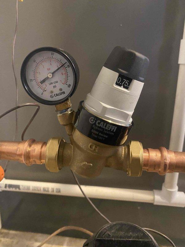 Responded to service call for water heater failure with no hot water production. Upon arrival, inspected 20-year-old tanked water heater unit that had reached end of serviceable life expectancy. Evaluated existing plumbing configuration including pressure regulation system with Calfi brass pressure regulator valve set at 0.75 PSI, pressure gauge assembly, and copper supply line connections with braided flexible connectors.

Assessed water heater installation including base mounting on gray platform, black vertical supply piping with red-handled brass shutoff valve, and dual port connections at unit base with red and blue indicators. Verified all plumbing connections, compression fittings, and metal clamps securing vertical pipe runs. Documented condition of existing low-lead compliant components and overall system configuration.

Given the age of the unit matching the home's 20-year construction date and repeated failure to maintain water temperature, recommended replacement as most co