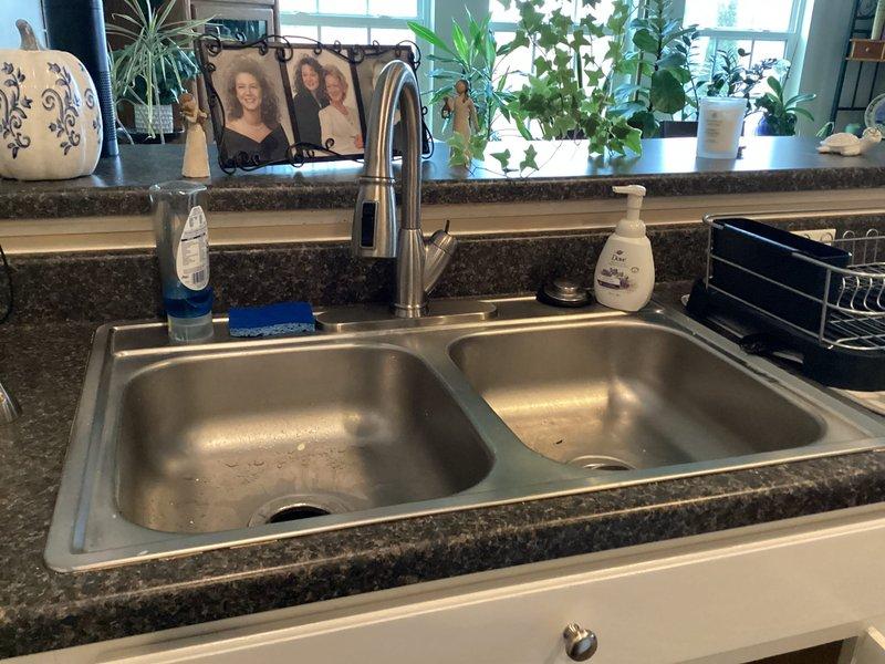 Completed plumbing membership inspection at residential property. Inspected bathroom angle stop valve and supply line connections for proper operation and leaks, verified toilet supply plumbing integrity. Examined kitchen double-basin sink, pull-down faucet assembly, and under-counter shut-off valves to ensure all fixtures were functioning correctly with no visible leaks or deficiencies.