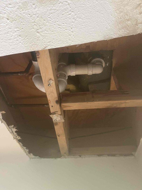 Returned to property to complete installation of tub waste and overflow assembly along with shower cartridge replacement that was previously sold. Accessed plumbing system through wall and ceiling openings to reach drainage and fixture components. Installed white PVC drainage piping with proper elbow fittings and connections for the tub waste and overflow system, securing all pipes to wooden framing members with metal brackets per code requirements. Replaced shower valve cartridge and verified proper operation of mixing valve. All plumbing connections were tested for leaks and proper drainage flow before completing the installation.