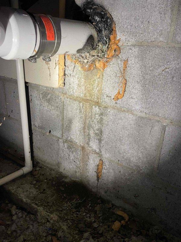 Responded to service call regarding sewer odor in bedroom potentially originating from crawlspace area. Upon inspection, discovered deteriorated pipe penetration through concrete block foundation wall with significant water damage, staining, and failed sealant material around entry point. Documented extensive moisture infiltration issues affecting wall integrity and PVC drainage system. Photographed complex sump pump discharge piping configuration showing multiple connections, elbows, and junctions with evidence of previous repairs. Identified compromised waterproofing at pipe penetration as likely source of odor infiltration into living space, with visible mold growth on foundation walls and inadequate sealing allowing sewer gases to migrate through crawlspace.
