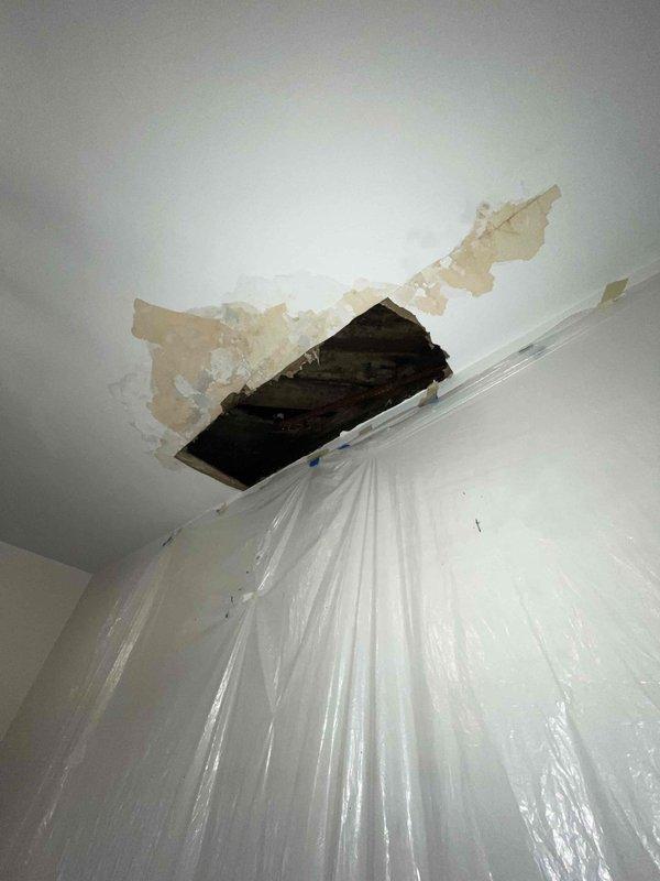 Responded to emergency call for ceiling leak originating from heating system piping. Upon arrival, found active water intrusion with extensive ceiling damage, including compromised drywall, significant water staining, and exposed structural members. Inspection revealed severely deteriorated wooden joists and beams with dark staining indicating prolonged moisture exposure and potential microbial growth. Located source of leak at corroded heating system pipe running through ceiling cavity.

Implemented immediate damage control measures by installing protective plastic sheeting to contain water flow and prevent further interior damage. Documented extensive deterioration of ceiling structure and heating pipe condition through photographic evidence. Advised customer of emergency nature of repairs needed and provided contact information for follow-up restoration work.