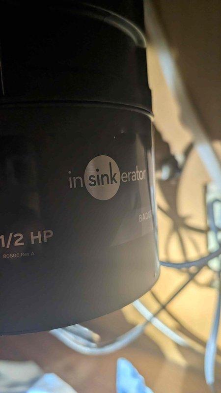 Responded to emergency call for leak under kitchen sink originating from garbage disposal. Upon arrival, inspected InSinkErator Badger 1/2 HP garbage disposal unit mounted beneath sink in fifty-year-old home. Located active leak at discharge elbow connection point on side of disposal unit. Identified worn gasket and loose mounting hardware as source of water intrusion into cabinet space. Tightened discharge tube connections, replaced deteriorated gasket, and verified proper seal at all connection points. Tested unit under running water to confirm leak was eliminated. Inspected electrical connections and power cord for safety compliance. Cleaned cabinet interior and removed standing water from base of cabinet. Unit restored to proper working condition with no further leakage detected.