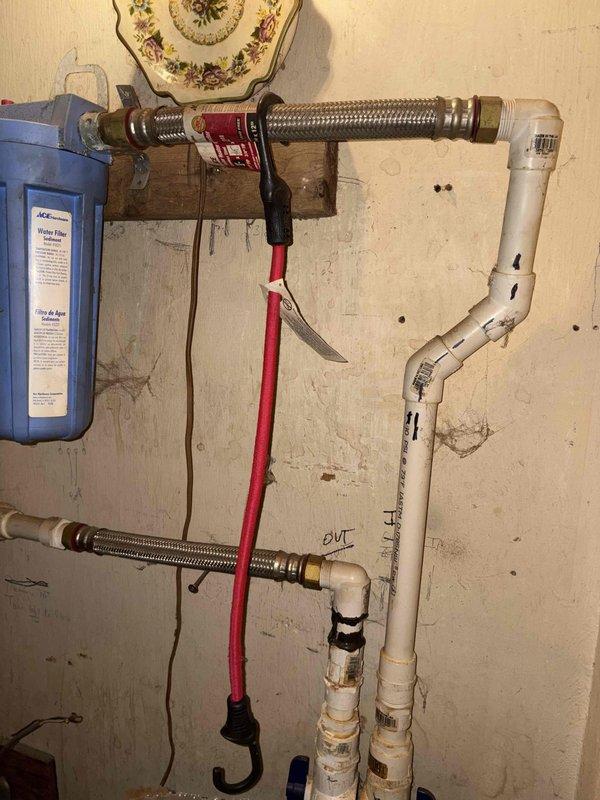 Responded to leaking valve located between water heater and water softener system. Diagnosed source of leak at valve connection point. Documented existing plumbing configuration including water filtration unit, PVC piping with marked flow directions, and flexible braided supply lines. Provided diagnostic assessment of valve failure and replacement recommendations to customer.