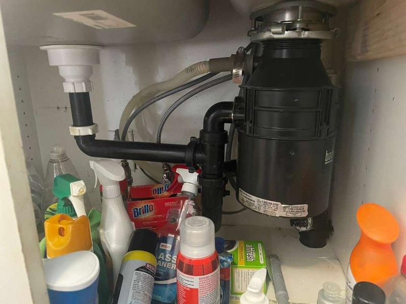Removed existing garbage disposal unit from double-basin kitchen sink and reconfigured the drain plumbing system. Disconnected the disposal from the mounting assembly and existing PVC drain lines, then installed new pipe configuration to restore proper drainage without the disposal unit. Cleared cabinet space of cleaning supplies to access plumbing connections, completed all pipe connections with appropriate fittings, and verified system integrity with no leaks detected upon testing.
