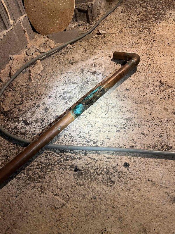 Responded to service call for multiple plumbing issues including leaking bathroom sink drain line and toilet losing water overnight. Upon inspection, discovered severely corroded 2-inch copper supply line in crawlspace area exhibiting extensive verdigris patching, indicating active deterioration and water seepage. Assessed PVC drain assembly beneath sink and identified compromised trap connection contributing to leak condition. Evaluated plumbing system configuration including garbage disposal mounting and drain routing. Documented corrosion damage to copper piping and deteriorated sections requiring replacement to restore proper water pressure and eliminate ongoing leak issues affecting both fixtures.