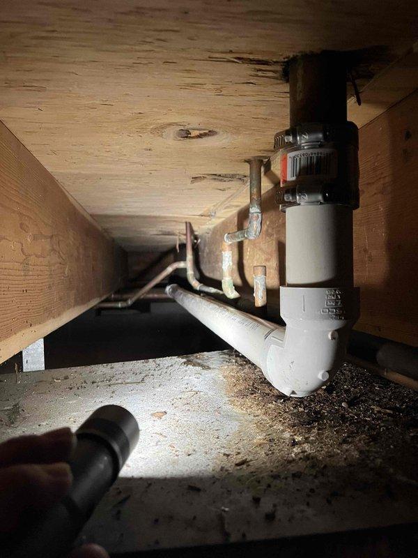 Responded to service call for multiple plumbing issues including leaking bathroom sink drain line and toilet losing water overnight. Upon inspection, discovered severely corroded 2-inch copper supply line in crawlspace area exhibiting extensive verdigris patching, indicating active deterioration and water seepage. Assessed PVC drain assembly beneath sink and identified compromised trap connection contributing to leak condition. Evaluated plumbing system configuration including garbage disposal mounting and drain routing. Documented corrosion damage to copper piping and deteriorated sections requiring replacement to restore proper water pressure and eliminate ongoing leak issues affecting both fixtures.