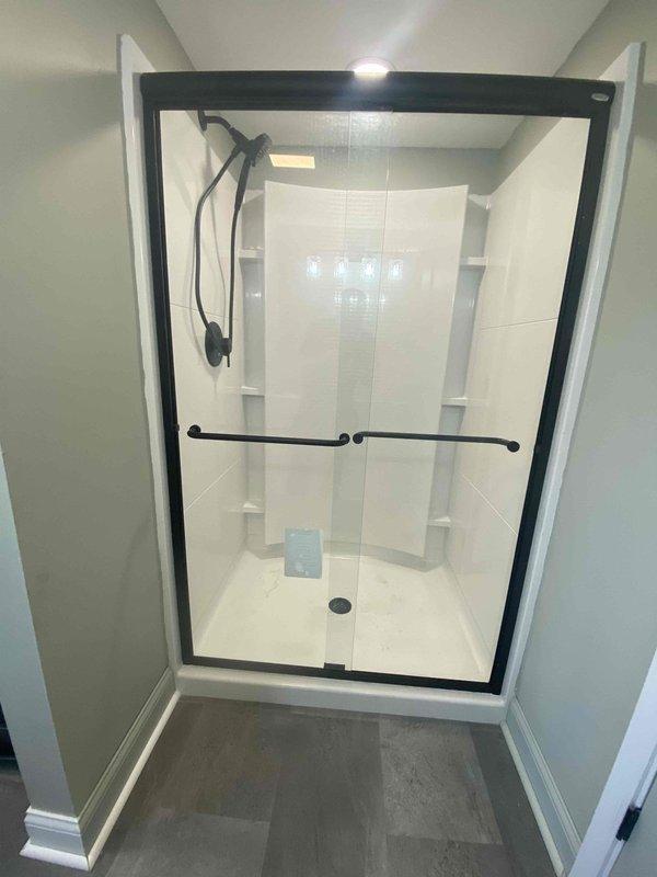 Completed return visit for finish plumbing work on bathroom and laundry installation. Installed and connected black-framed glass shower enclosure with handheld showerhead system, safety grab bar, and all associated fixtures. Connected front-loading washing machine with proper venting and electrical hookups in designated laundry alcove.