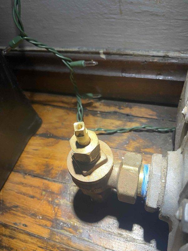 Returned to property to investigate reported leak on upstairs boiler unit. Upon inspection, identified moisture and water damage on wooden platform beneath boiler system. Located source of leak at brass T-joint valve fitting with compression-style connection. Valve showed signs of wear and minor seepage at threaded connection points. Inspected surrounding piping infrastructure, including insulated supply lines and associated ductwork. Documented conditions with photographs showing valve assembly, connection points, and water-damaged areas for service records. Recommended valve replacement and platform repair to prevent further deterioration and ensure system integrity.