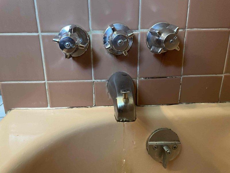 Responded to service call for leaking faucets in both bathroom and kitchen. Inspected vintage three-handle tub/shower valve assembly with chrome cross-handle fixtures and tub spout in bathroom with pink tile surround. Assessed kitchen dual-handle chrome faucet with high-arc spout mounted on stainless steel sink. Identified worn valve seats and deteriorated washers causing drips in both locations. Replaced faulty components, tested water flow and temperature control on all handles, and verified complete leak elimination at both fixtures.