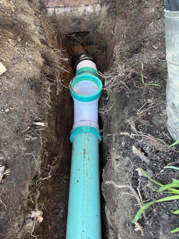Completed spot repair of sewer cleanout system in excavated trench. Removed damaged piping section and installed new PVC pipe connections with proper coupling fittings, transitioning from existing turquoise pipe to white PVC segments. Excavation depth measured and verified for code compliance before backfilling and site restoration.