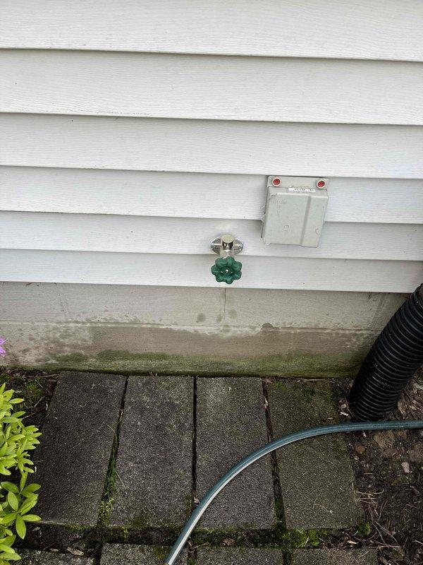 Completed installation of outdoor water spigot with proper mounting hardware and cover plate on exterior wall with vinyl siding. Verified proper operation of spigot with green cross-handle valve and confirmed secure hose connection without leaks.