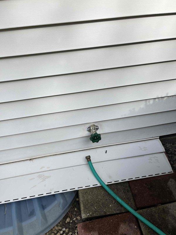 Completed installation of outdoor water spigot with proper mounting hardware and cover plate on exterior wall with vinyl siding. Verified proper operation of spigot with green cross-handle valve and confirmed secure hose connection without leaks.