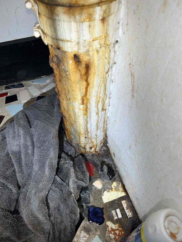 Responded to service call for severely corroded basement stack pipe requiring assessment and quote. Upon arrival, inspected exposed vertical drain stack with T-fitting connection serving kitchen drain line. Primary vertical section displayed extensive rust deterioration and corrosion throughout approximately 5 feet of pipe length, with heavy orange-brown oxidation, surface pitting, and structural compromise evident along the entire run. Corrosion was most severe in middle and lower sections where rust had penetrated deeply into pipe walls, creating significant risk of failure and potential water damage.

Documented condition of stack pipe showing rust streaking, wall discoloration, and moisture staining around pipe area indicating possible intermittent leaking. Assessed T-fitting junction point connecting to kitchen drain and evaluated structural integrity of corroded vertical section extending downward to base connection. Photographed deteriorated pipe sections, exposed basement utili