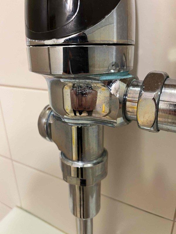 Responded to customer complaint of fluctuating water pressure in a fifteen-year-old residential property. Upon arrival, conducted comprehensive assessment of the plumbing system to identify the source of pressure inconsistencies.

Performed visual inspection of accessible plumbing fixtures and supply lines throughout the property. Examined chrome-plated fixture assembly at sink location, identifying significant mineral deposits and corrosion on brass connector nut and compression fittings. The buildup of scale and sediment on these components was contributing to restricted water flow and pressure variations.

Inspected main water supply system in utility area, documenting condition of PVC drainage and supply piping configuration. Evaluated the complex arrangement of pipes including multiple elbow joints and vertical/horizontal sections for potential flow restrictions or blockages. Assessed white metal utility cabinet housing plumbing connections for any signs of leaks or system degrada
