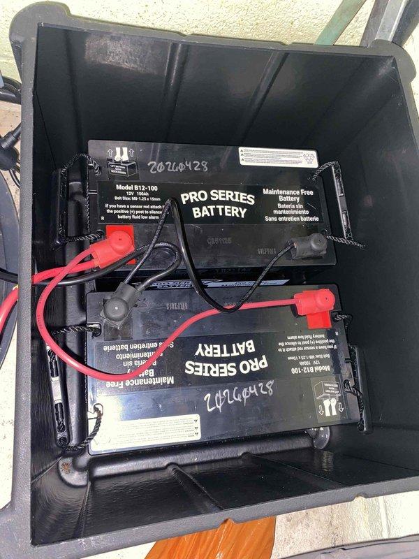 Completed installation of backup power system components including two Pro Series Model B12-100 maintenance-free batteries in vertical stacked configuration within dedicated battery compartment. Installed electronic control unit with illuminated display panel mounted on molded platform base against utility room wall. Connected heavy-gauge battery cables with proper terminal connections and installed dual antenna configuration on control unit. Routed flexible corrugated conduit for ventilation and cable management. System tested and operational upon completion of two-hour installation following arrival of ordered materials.