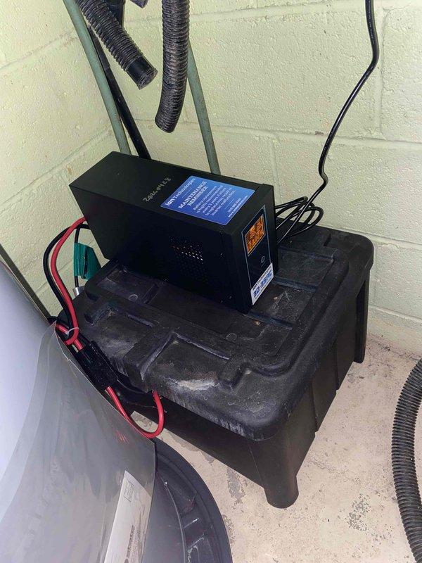 Completed installation of backup power system components including two Pro Series Model B12-100 maintenance-free batteries in vertical stacked configuration within dedicated battery compartment. Installed electronic control unit with illuminated display panel mounted on molded platform base against utility room wall. Connected heavy-gauge battery cables with proper terminal connections and installed dual antenna configuration on control unit. Routed flexible corrugated conduit for ventilation and cable management. System tested and operational upon completion of two-hour installation following arrival of ordered materials.