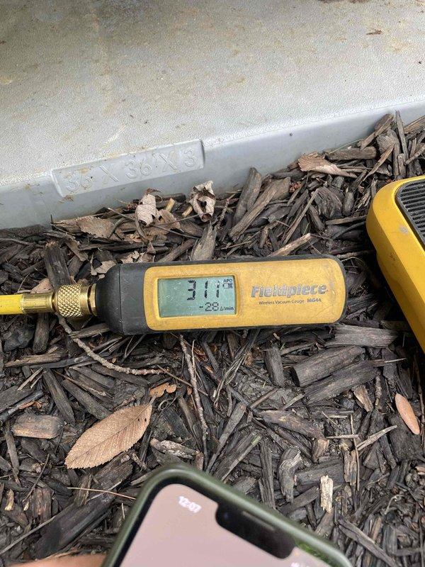 Returned to system to perform pressure test and leak detection as previously sold. Connected Fieldpiece SMAN refrigerant manifold and micron gauge to R410A system to conduct comprehensive diagnostic testing. System pressures measured at 116.7 PSI on low side and 203.5 PSI on high side with superheat reading of 10 degrees and subcool of 24 degrees. Performed deep vacuum test using Fieldpiece MG44 wireless vacuum gauge, achieving -28.3 Hg vacuum reading of 31.1 microns to verify system integrity and identify potential refrigerant leaks in the outdoor condensing unit.