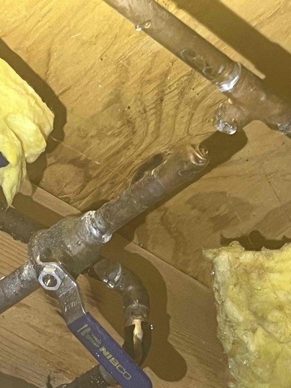 Responded to service call for broken water line supplying outdoor spigot. Upon arrival, found main water supply to residence had been shut off due to active leak. Inspected basement plumbing system and traced supply line to outdoor spigot through ceiling joists in utility area. Located compromised section of pipe in ceiling space showing severe corrosion and frost accumulation, indicating prolonged moisture exposure and failure point. Pipe exhibited significant surface deterioration with oxidation throughout affected section. Assessed damage and determined section of water line required replacement to restore service to outdoor spigot and allow main water supply to be safely restored to residence.