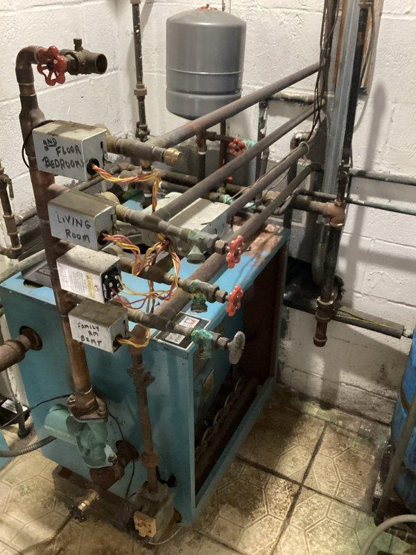 Responded to no-heat call for gas-fired hydronic boiler system. Upon arrival, inspected multi-zone heating distribution manifold with turquoise base frame serving multiple areas including second floor bedrooms, living room, and family room zones. Evaluated boiler unit, associated copper piping network, expansion tank, and zone valves with red handles throughout the manifold assembly. Documented existing system configuration showing signs of age with visible corrosion on piping components. Provided estimate for necessary repairs to restore heating system operation.