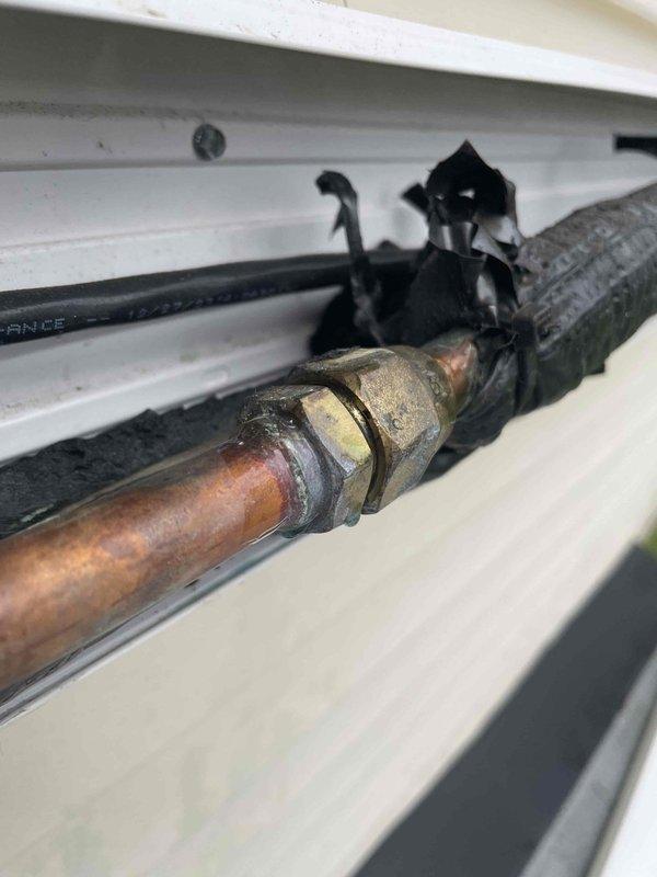 Responded to service call for mini split system displaying error code indicating refrigerant leak, consistent with previous issue from last spring. Upon inspection, identified compromised copper refrigerant line connections at exterior unit showing significant corrosion and weathering on compression fittings. Documented condition of copper piping and brass union connections displaying oxidation and patina from environmental exposure. System requires refrigerant leak repair at corroded connection points and complete refrigerant recharge to restore proper operation.