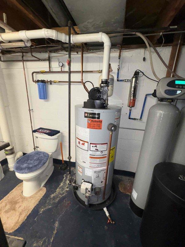 Responded to service call for leaking water treatment system and water heater previously installed in March 2023. Inspected A.O. Smith water heater with mounted circulation pump, gray water softener/filtration system with digital control head, pressure tank, and associated copper and PVC plumbing connections in basement utility area. Documented equipment condition and identified source of water treatment system leak. Assessed overall system performance including blue water filter housing, piping connections, and mechanical components to determine necessary repairs.