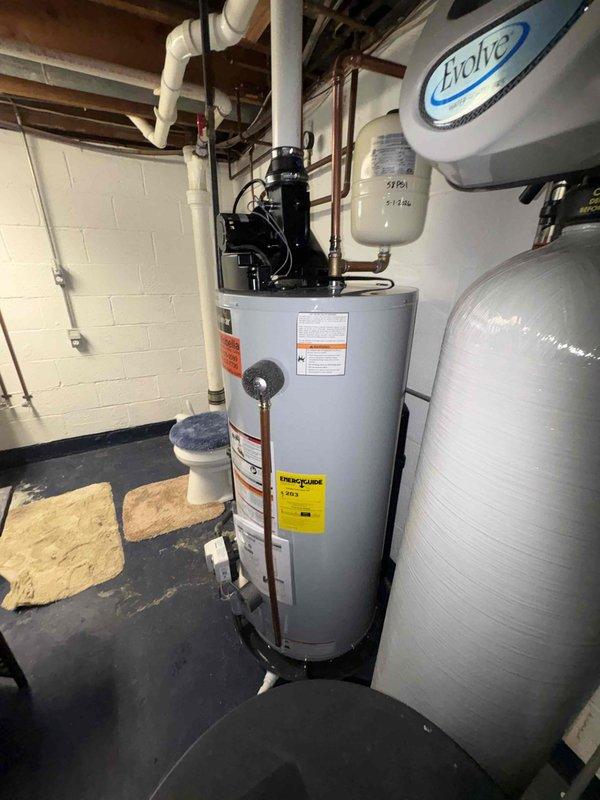 Responded to service call for leaking water treatment system and water heater previously installed in March 2023. Inspected A.O. Smith water heater with mounted circulation pump, gray water softener/filtration system with digital control head, pressure tank, and associated copper and PVC plumbing connections in basement utility area. Documented equipment condition and identified source of water treatment system leak. Assessed overall system performance including blue water filter housing, piping connections, and mechanical components to determine necessary repairs.